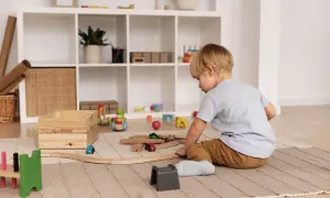 Chłopiec bawi się drewnianą kolejką na dywanie w pokoju dziecięcym.