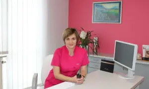 Lekarka w różowym uniformie siedzi przy biurku w gabinecie estetycznym.