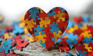 Serce z puzzli w kolorach czerwonym, żółtym i niebieskim, otoczone luźnymi elementami.