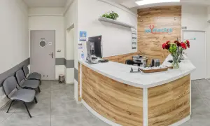 Recepcja kliniki medycznej z ladą, komputerem, krzesłami i bukietem kwiatów.