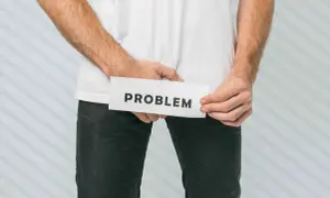 Mężczyzna trzyma kartkę z napisem "PROBLEM" w okolicy krocza.