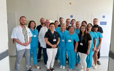 Grupa lekarzy i pielęgniarek w uniformach medycznych pozuje do zdjęcia w szpitalnym korytarzu.