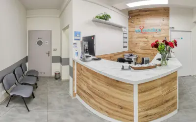 Recepcja kliniki medycznej z ladą, komputerem, krzesłami i bukietem kwiatów.