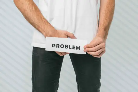 Mężczyzna trzyma kartkę z napisem "PROBLEM" w okolicy krocza.