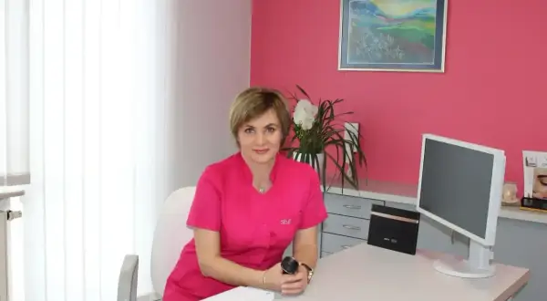 Lekarka w różowym uniformie siedzi przy biurku w gabinecie estetycznym.