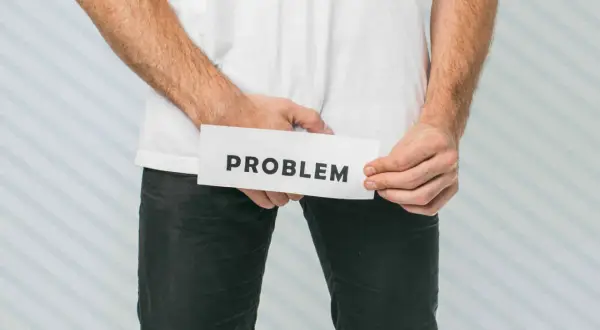 Mężczyzna trzyma kartkę z napisem "PROBLEM" w okolicy krocza.