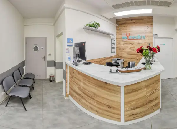 Recepcja kliniki medycznej z ladą, komputerem, krzesłami i bukietem kwiatów.